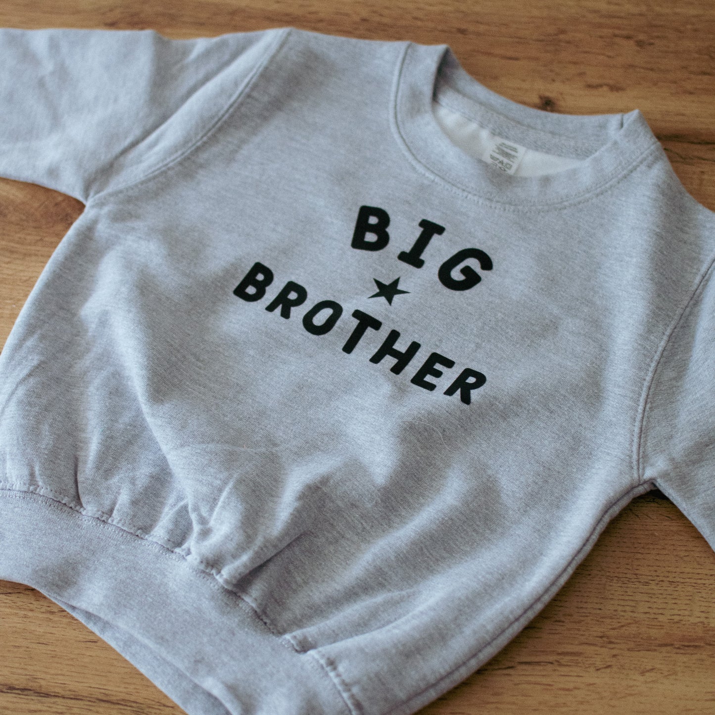 Grey sweatshirt with 'BIG BROTHER' text on a wooden surface