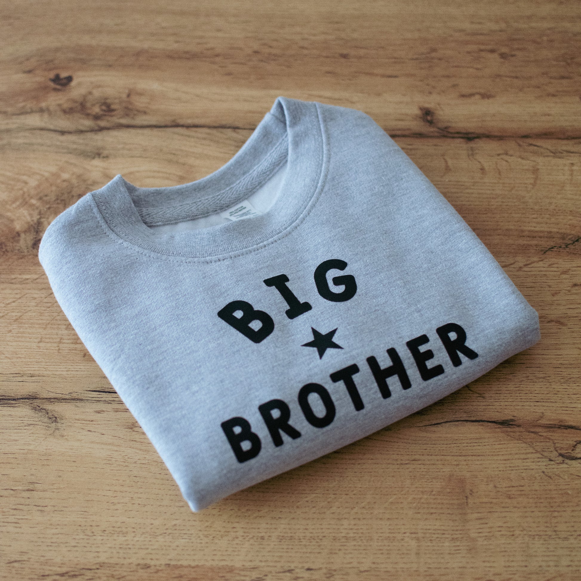 Folded grey sweatshirt with 'BIG BROTHER' text on a wooden surface