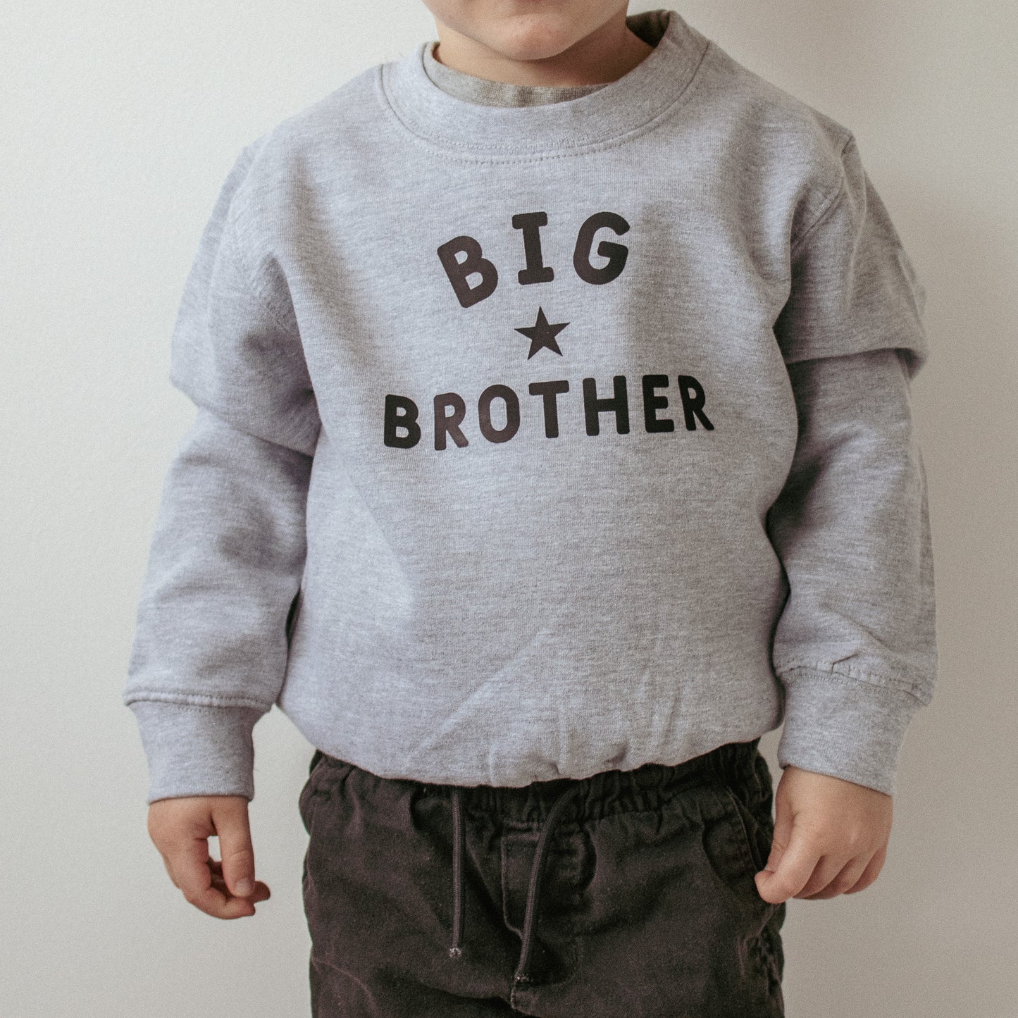 Child wearing a grey sweatshirt with 'BIG BROTHER' text on a plain background